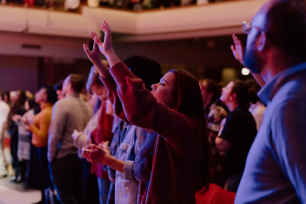 A women with her hands raised in worship at Founder's Week, a free bible conference from Moody Conferences