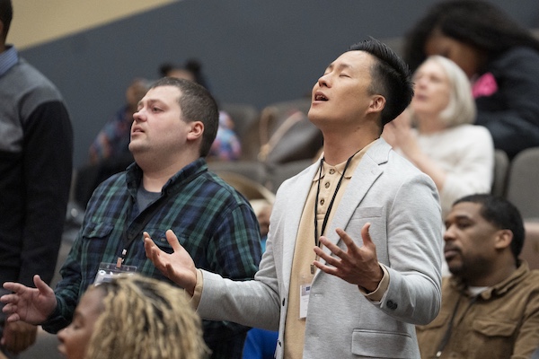 Conference attendees raising their hands in worship at a conference presented by the Center for Compelling Biblical Preaching at Moody Theological Seminary